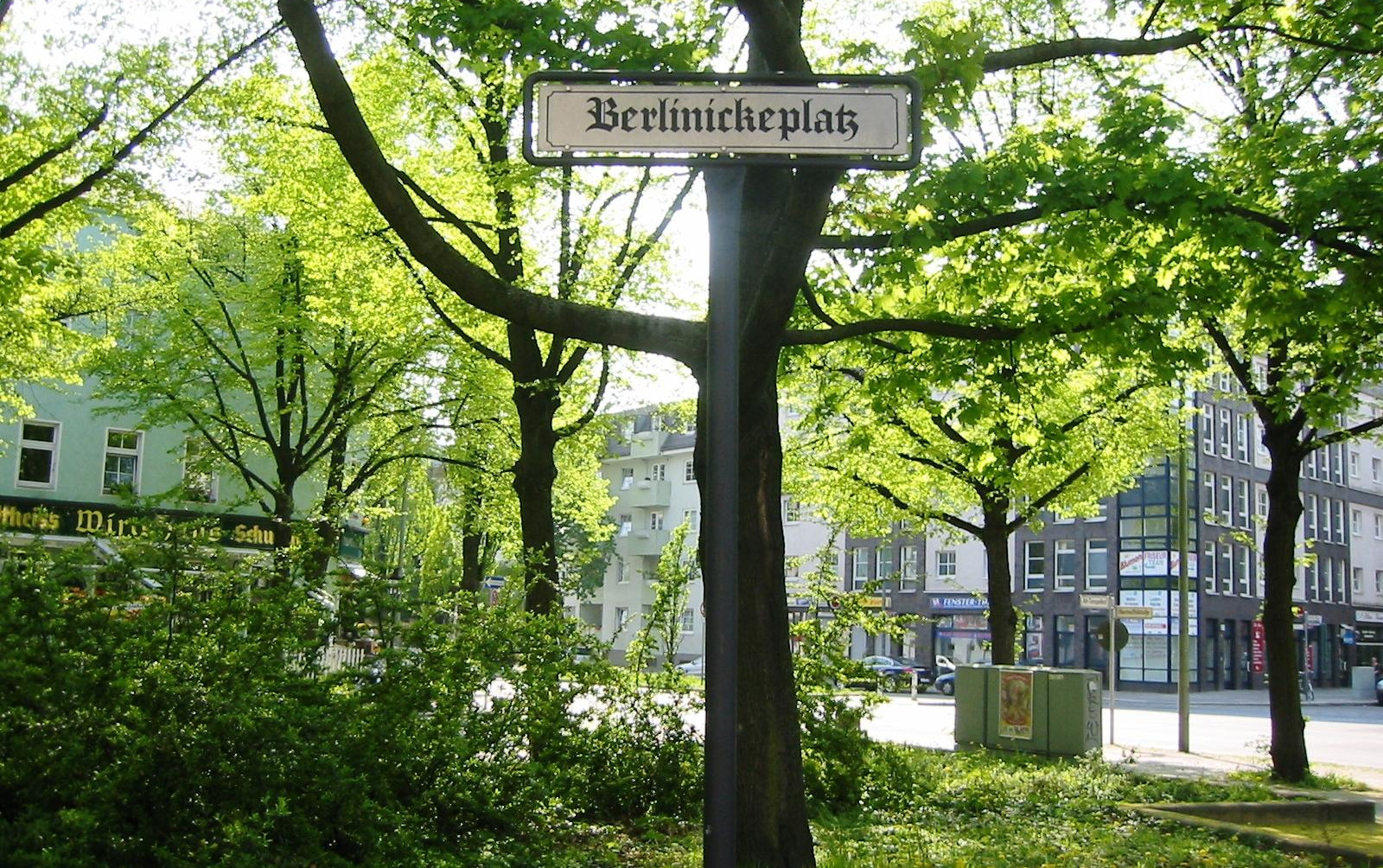 Bäume und viel Grün. Im Vordergrund ein Straßenschild "Berlinikeplatz".